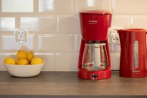 A close-up of the kitchen counter featuring a vibrant red coffee maker, kettle, and a bowl of fresh lemons, adding a cheerful touch.

