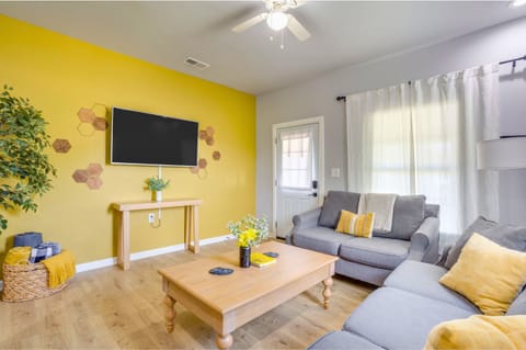 Bright living room with yellow accent walls, Smart TV, sectional sofa with bee-themed décor, and natural light throughout.