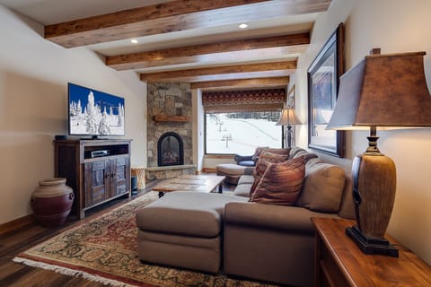 Unwind in your cozy living room with exposed beams, stone fireplace, and mountain views—perfect for après-ski relaxation.