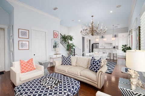 Relax in your bright, stylish living room with plush sofas, elegant chandelier, and open-concept flow to the modern kitchen.