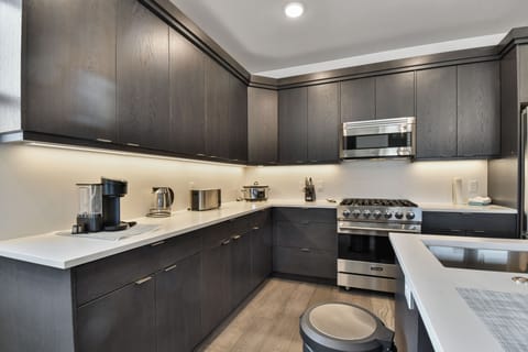 This sleek modern kitchen features premium Viking stainless steel appliances, dark cabinetry with clean lines, and bright under-cabinet lighting. The streamlined design offers ample counter space, making it both stylish and highly functional.