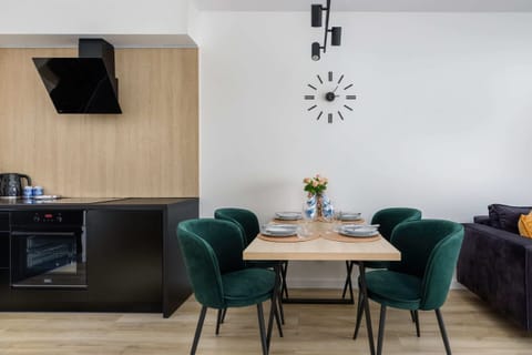 A modern open kitchen equipped with black cabinets, a built-in oven, and a small dining area with green chairs.