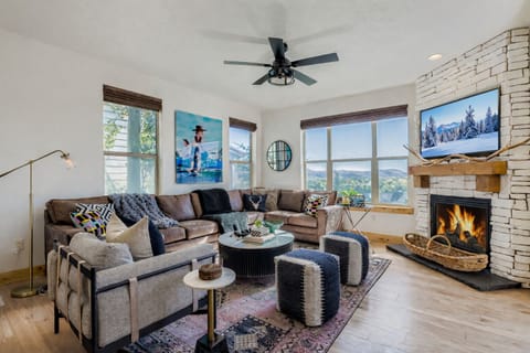 This sun-drenched living area features a white brick corner fireplace, plush seating, and expansive windows. Enjoy breathtaking mountain and golf course views while relaxing in this modern, cozy retreat.