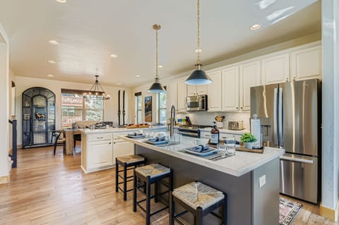 This gourmet kitchen features a large contrast-colored island with stone countertops and industrial pendant lighting. Perfect for entertaining, it offers high-end stainless appliances and seamless open-plan flow.