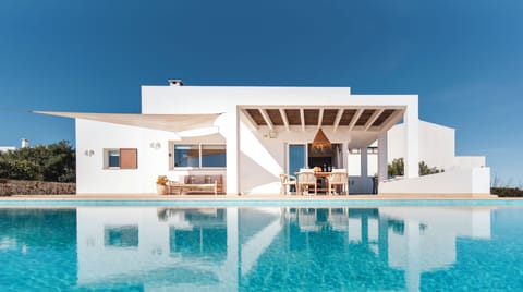 Piscina y fachada frontal de la villa, con terraza cubierta con comedor exterior