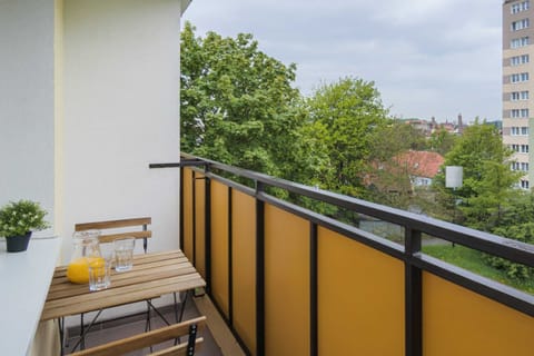 A balcony with a yellow railing and a view of greenery and surrounding buildings.