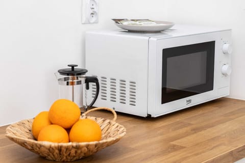 A kitchen nook with white cabinets, a microwave, and a decorative basket of fresh oranges.