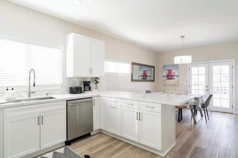 This kitchen and dining space blends modern elegance with coastal charm. The dining area features a contemporary chandelier and bright artwork, adding a pop of color and personality. Plus, those French doors bring in plenty of natural light!