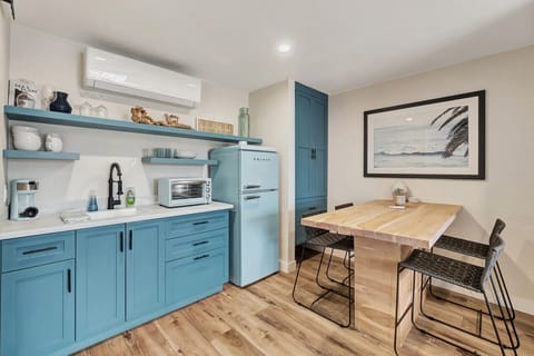 Bright kitchenette w/ blue cabinets, retro-style fridge & wood dining table for casual meals