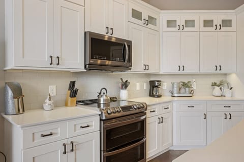 Open kitchen w/ stainless appliances, white cabinets, modern sleek design.