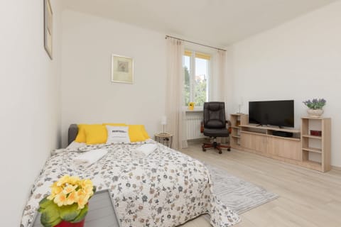 A cozy sleeping space with a double sofa bed, decorated with yellow cushions and floral bedding, with a small desk in the background.