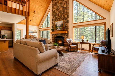 Sink into plush sofas by the crackling stone fireplace, where soaring windows frame forest views and vaulted wood ceilings create your perfect mountain sanctuary.