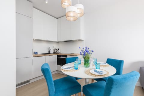 A sleek kitchenette with white cabinetry, integrated appliances, and a round dining table set with four blue chairs.