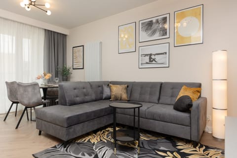 The living room is spacious and modern, featuring a large gray sofa with decorative pillows and a stylish black coffee table. The walls are decorated with framed artwork, and a floor lamp adds to the cozy ambiance.