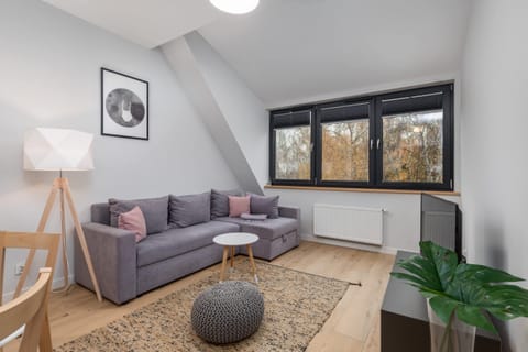 A cozy living room with a grey sofa, a woven coffee table, and large windows offering a scenic outdoor view.
