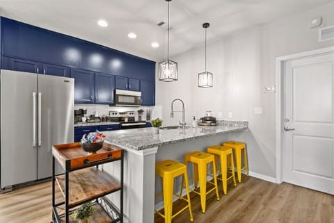 This kitchen boasts a bold and cheerful aesthetic with its bright blue cabinetry, vibrant yellow bar stools, and sleek granite countertops.