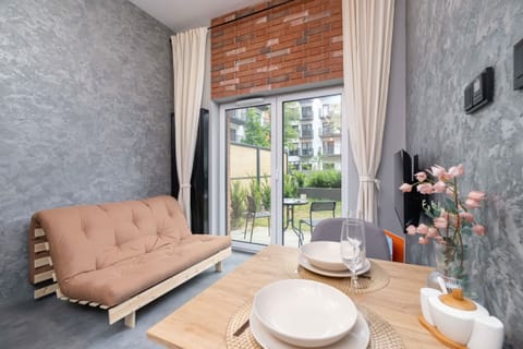 A cozy dining area with a wooden table, beige sofa, and large window offering a garden view.

