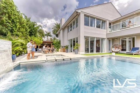 Outdoor Heated Pool with Waterfall feature, separate Hot Tub, Cabana, BBQ and Lounge Chairs all covered in artificial turf. 