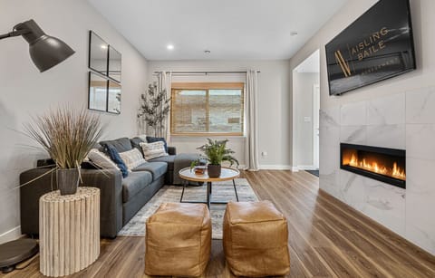 Living room, located on the main floor, with an electric fireplace, Smart TV, cozy sectional, and walkout access to the backyard.