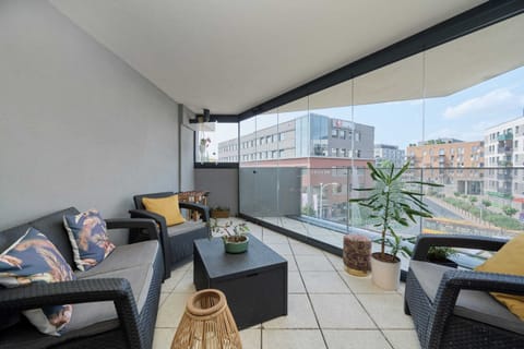 A spacious balcony with cozy seating, decorated with pillows and overlooking the city.

