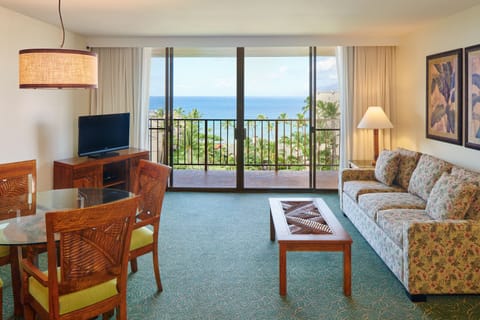 Step into your bright living room where ocean views stretch beyond your private balcony. Unwind on the cozy sofa or gather around the dining table, all while enjoying the tropical paradise just outside your door.