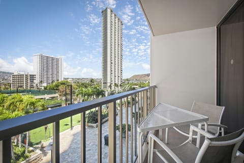 A covered balcony overlooks lush tropical landscaping, urban towers, and a distinctive volcanic peak in the distance, marking your arrival in a vibrant island neighborhood.