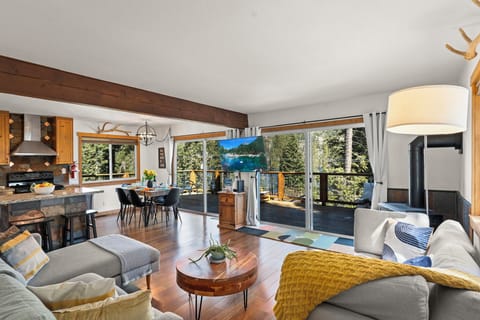 Relax in your open-concept living space with stunning forest views through floor-to-ceiling windows. The cozy fireplace and modern kitchen create perfect mountain retreat vibes.