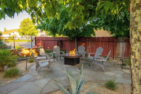 This charming stone patio features a modern fire pit and comfortable Adirondack seating, all nestled under a lush canopy of trees for the ultimate evening retreat.