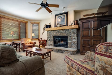 Cozy up in your spacious living room with a stone fireplace, plush seating, and warm wood accents creating the perfect mountain retreat atmosphere.