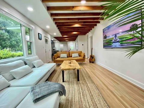 Step into the spacious living room with a vibrant Majesty Palm, where the eye is drawn upward to the striking exposed ceiling beams, creating a harmonious blend of nature and architectural charm. 