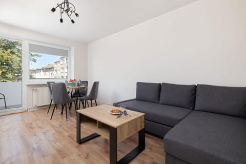 Bright living room with a grey sofa, wooden coffee table, and large windows letting in natural light.

