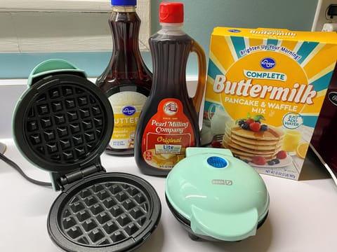 Waffle station with waffle mix and syrup provided. 