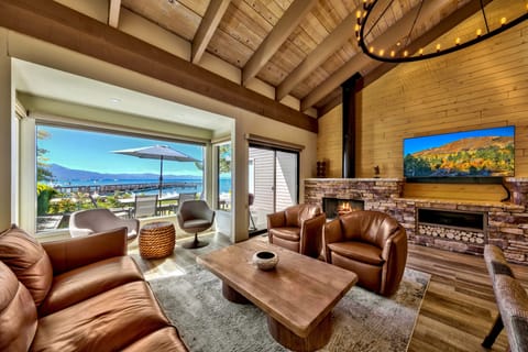 Unwind in your stunning mountain retreat with leather seating, stone fireplace, and breathtaking lake views through expansive windows.