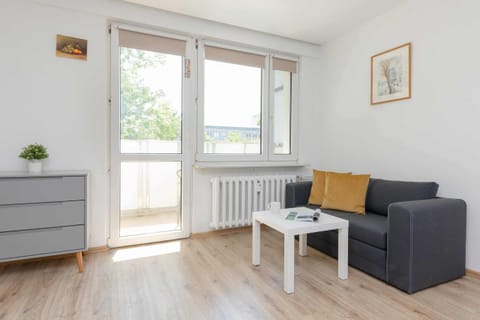 A bright living area with a gray sofa, a small coffee table, and large windows letting in natural light.

