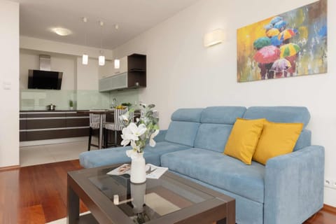 A modern living room with a blue sofa, yellow cushions, a coffee table, and a TV unit, creating a cozy yet vibrant atmosphere.

