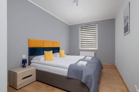 A bright bedroom with a comfortable bed featuring a vibrant yellow and blue headboard and minimalistic decor.

