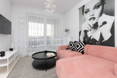 A stylish living room featuring a pink sofa, black-and-white decor accents, and modern art on the wall.

