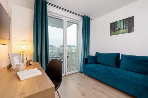 A bright living room with a teal sofa, a desk by the window, and natural light streaming in.

