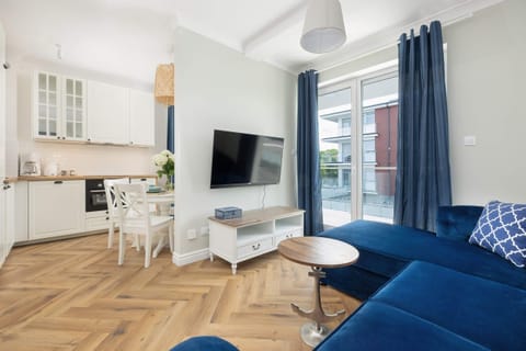 A bright living space featuring a navy sofa, large windows, and airy curtains.

