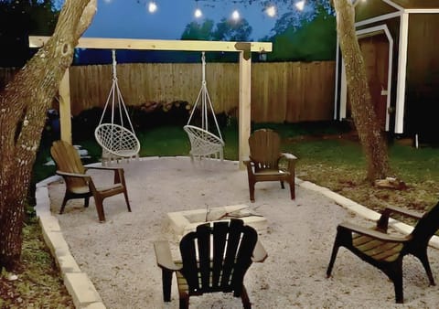 Fire pit area with string lights, hanging chairs, Adirondacks, and trees