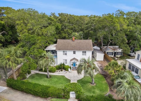 Aerial view of a charming white two-story property nestled among lush tropical landscaping and mature trees, situated in a peaceful residential neighborhood.
