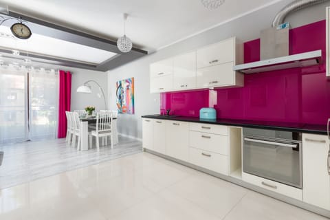 A contemporary kitchen with white cabinetry, high-gloss pink backsplash, and state-of-the-art appliances for a functional yet stylish look.