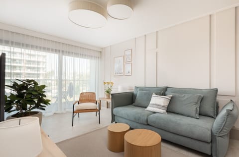 A bright living room with a modern design, featuring a comfortable gray sofa and large windows overlooking greenery.