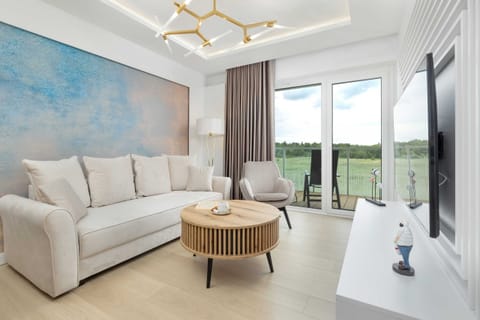 A bright and spacious living room featuring a cozy white sofa, a stylish round coffee table, and large windows offering a scenic view.