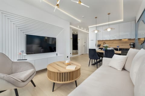 A well-lit living room with a large TV, comfortable furnishings, and a bright atmosphere for relaxation and entertainment.