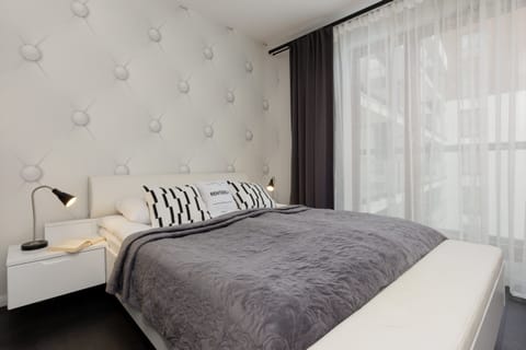 A cozy bedroom with a tufted headboard, soft gray bedding, and large windows for a bright and relaxing atmosphere.

