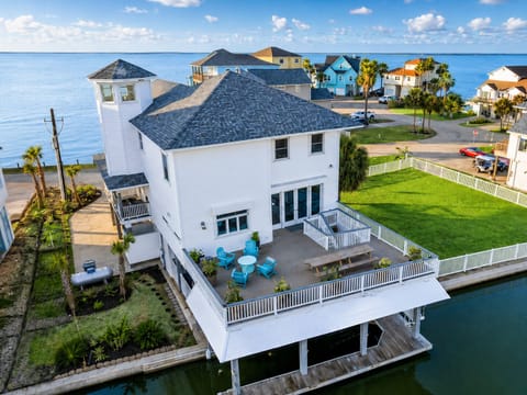 Aerial view of canal-front Galveston vacation home with private dock, fenced lawn, deck seating, and waterfront views.
