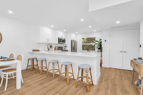 There are 5 sky-blue rattan bar stools at the impressively large quartz kitchen counter. The kitchen also has a kitchen nook with 2 upholstered rattan and cane benches, a modern contemporary white round table, and a decorative Fiddle tree.
