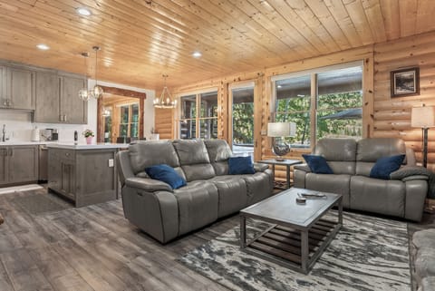 - Open concept living room with cabin wood accents and leather sofas  
- Large windows bring natural light and peaceful forest views inside  
- Relax in comfort after outdoor adventures in the mountains