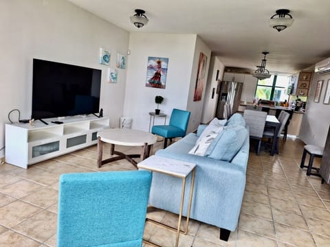 Large living room, sleep sofa and 65” 4K TV with dining room in the background.